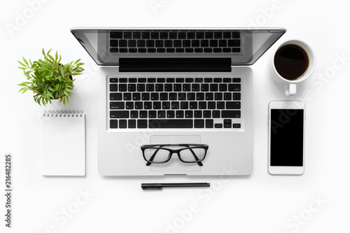 White office desk table with laptop computer, smartphone, cup of coffee, notebook and supplies. Top view, flat lay.