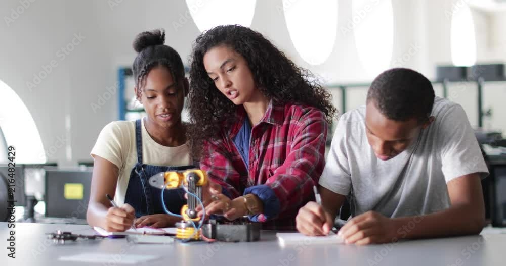 High school students working on a robotic arm in class High school students working on a robotic arm in class