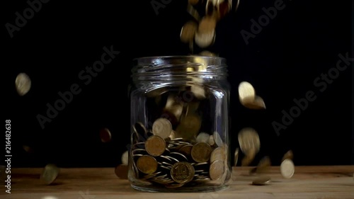 Slow motion, a pile of coins falls into an empty glass jar on a black background. Ukrainian coins fall into a jar.