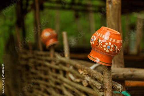Clay vintage traditional pot on the fence. Rural landscapes, traditional old clay pots on a wicker fence. Ceramic pitcher on the fence, a village tradition in Ukraine, in Russia. © Aleksandr Lesik