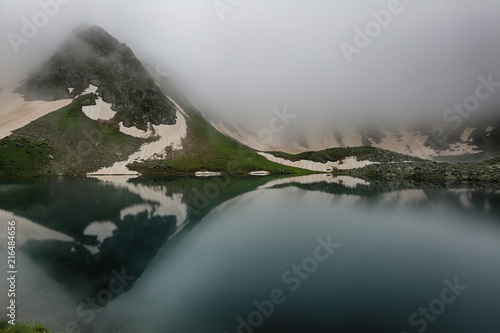 Caucasian mountains in the fog at sunrise with reflection in the lake