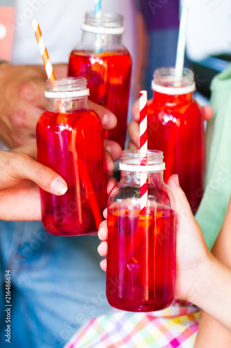 Picnic theme: happy young family  holding drinks, toast bottle with red juice , close-up