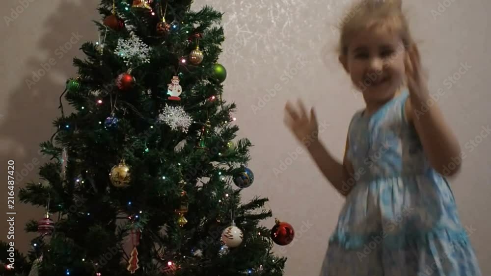The child jumps and claps in anticipation of Christmas and the new year. Little girl decorating christmas tree with toys and balls. The child jumps and claps in anticipation of Christmas and the new year. Little girl decorating christmas tree with toys and balls.