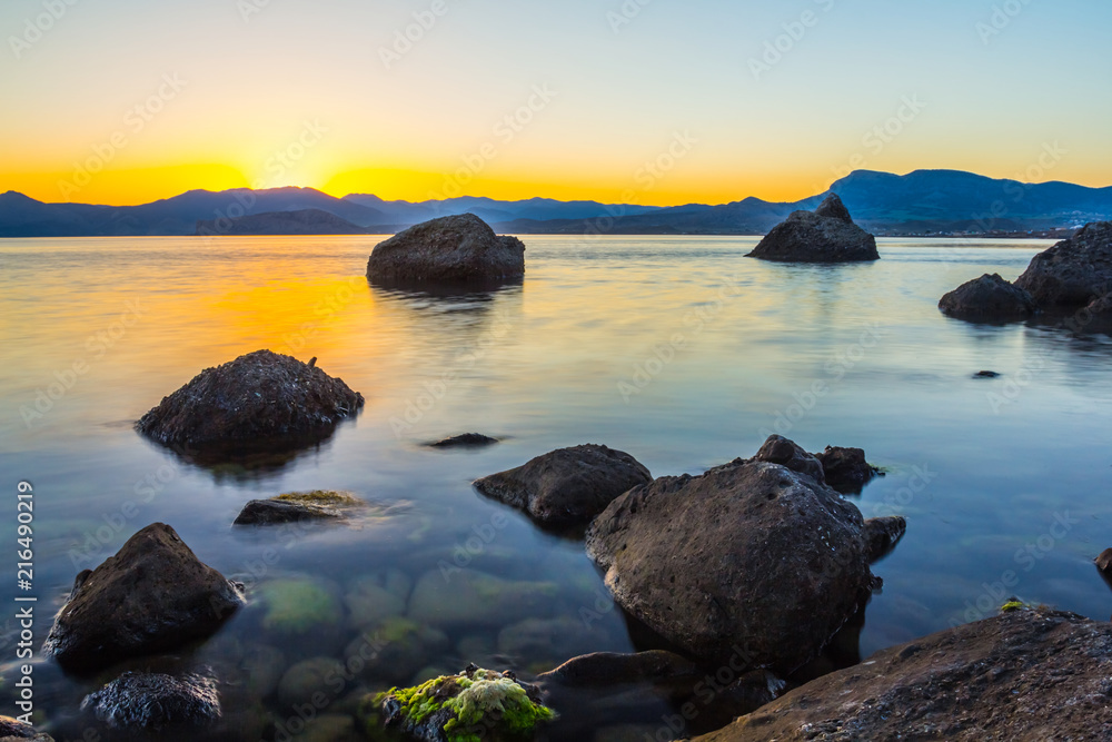 quiet sea bay with stones in a water at the sunset