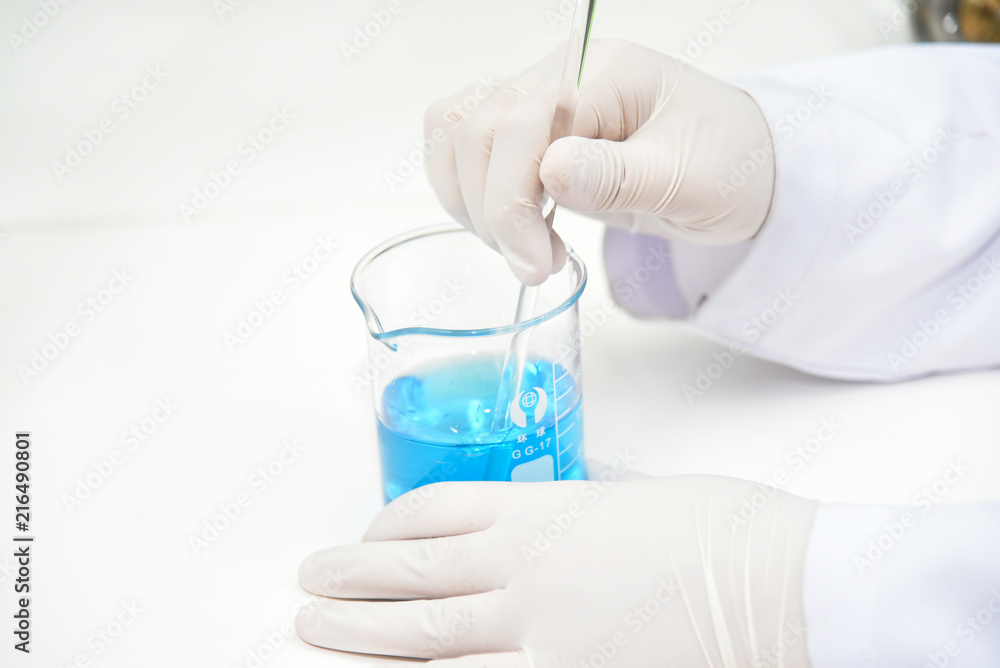 Close up female hands of the scientist mixing blue liquid in a beaker
