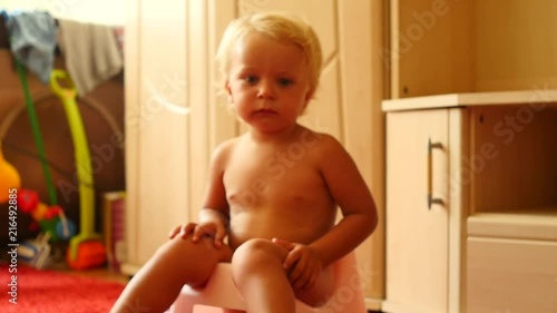 cute blond 1,5 years old baby boy on chamberpot indoors approaching camera