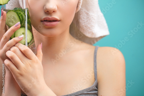 Cropped view of urecognizable female face with towel on head pressing tightly to her cheel glass of cold cucubmer and mint coctail. Beauty salon concept. Skin and hair care. photo
