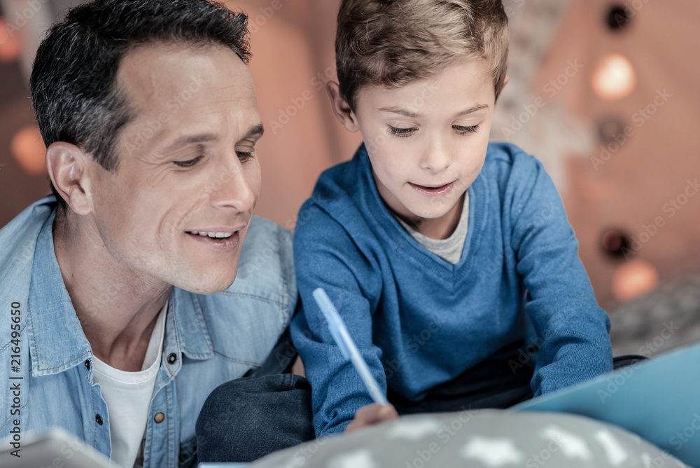 Be attentive. Concentrated boy making notes while sitting near his daddy Be attentive. Concentrated boy making notes while sitting near his daddy