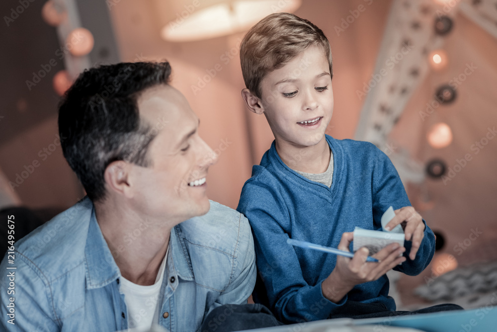 For notices. Pleased male person keeping smile on his face while spending time with his kid For notices. Pleased male person keeping smile on his face while spending time with his kid
