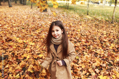 Closeup portrait of cute adorable smiling little caucasian girl child standing in autumn fall park outside, looking in camera,