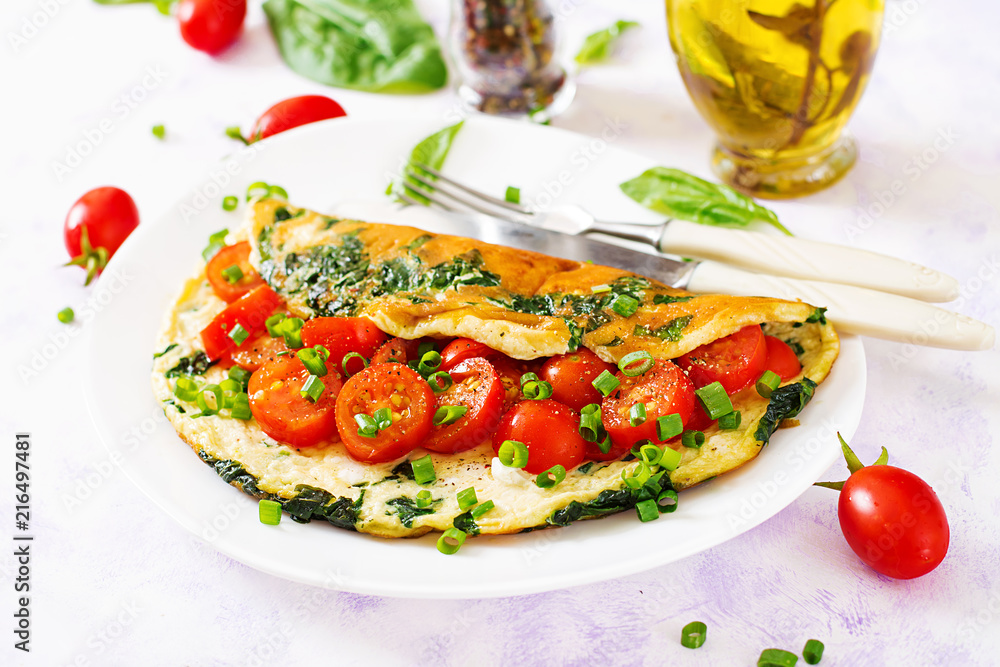 Omelette with tomatoes, spinach and green onion on white plate.  Frittata - italian omelet.