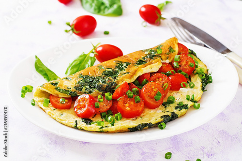 Omelette with tomatoes, spinach and green onion on white plate.  Frittata - italian omelet.