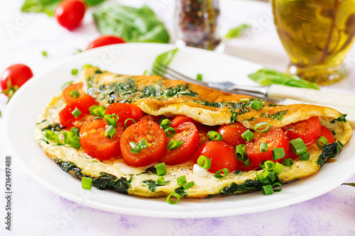 Omelette with tomatoes, spinach and green onion on white plate. Frittata - italian omelet.