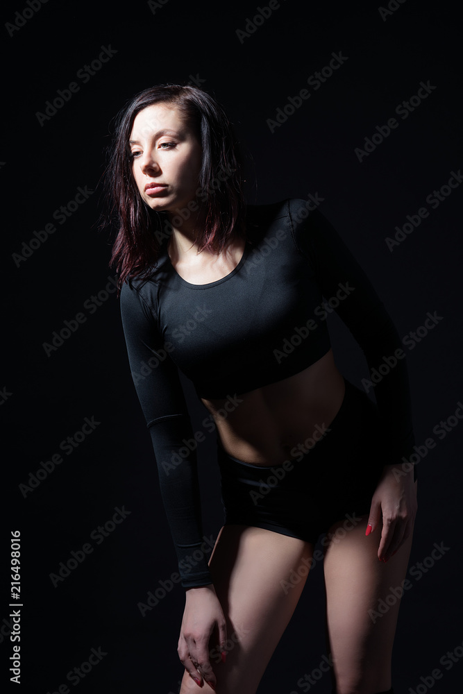 Sports girl in black top and shorts in a dance position on a black isolated background. Female portrait in a low key. Sports girl in black top and shorts in a dance position on a black isolated background. Female portrait in a low key.