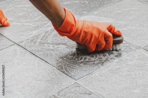 Hand of man wearing orange rubber gloves is used to convert scrub cleaning on the tile floor.