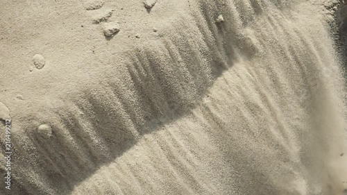 White fine sand avalanche slopes down the hill under sun light on sea, ocean, river coast or in desert. Abstract summer surface background. Closeup view. Slow motion