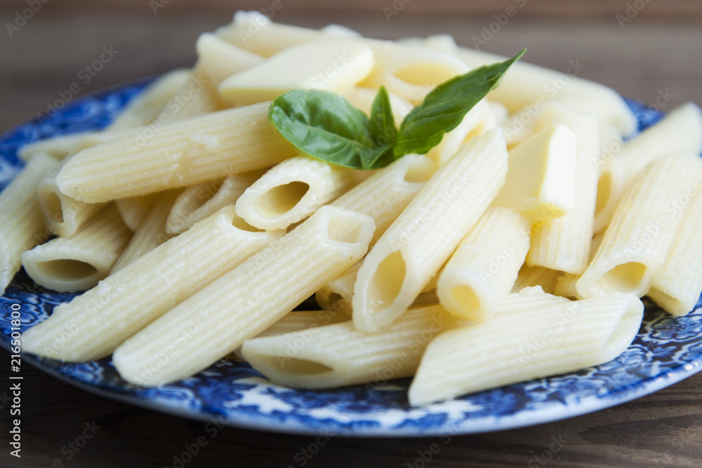 Cooked penne pasta with butter, cheese and basil in vintage beautiful blue plate on wooden table. Cooked penne pasta with butter, cheese and basil in vintage beautiful blue plate on wooden table.