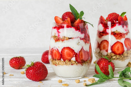 strawberry yogurt parfait with granola, mint and fresh berries in glasses on white wooden table. healthy breakfast