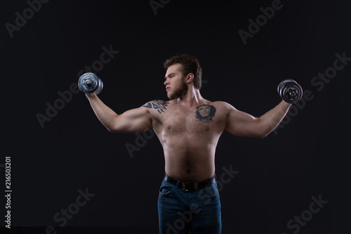 Muscular bodybuilder guy doing exercises with dumbbells over black background