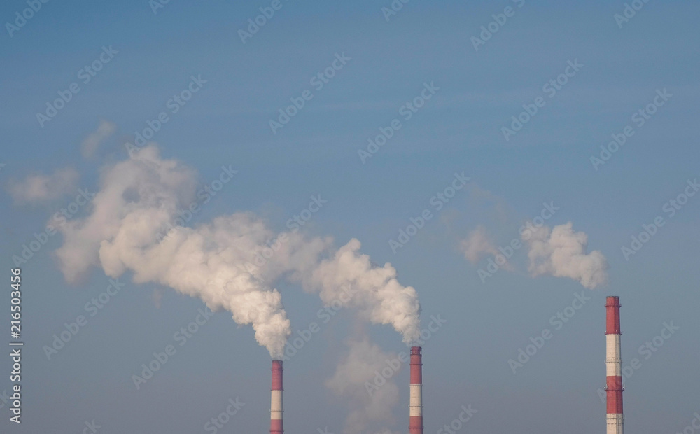 Three red and white pipes of thermal power station with smoke in sky and tree background. Three red and white pipes of thermal power station with smoke in sky and tree background.