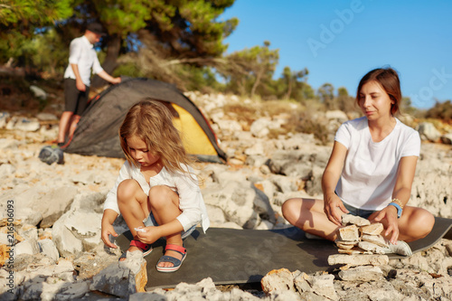 Mom and little girl imposes stone one by one at beach.