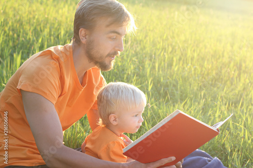 Father and his toddler son read book together outdoor. Copy cpace