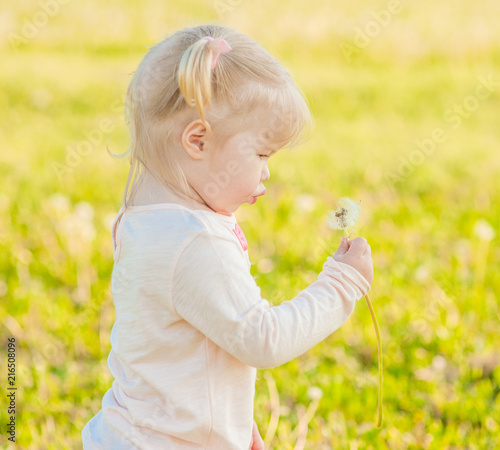 Baby girl blowing a dandelion in the rays of the setting sun