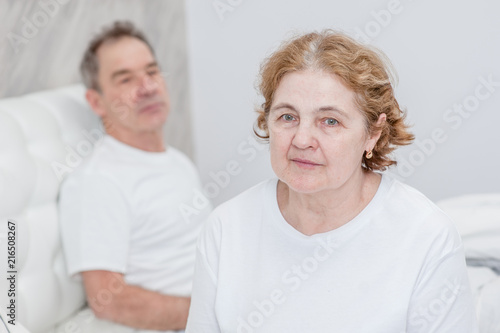 Sad senior couple sitting on bed at home