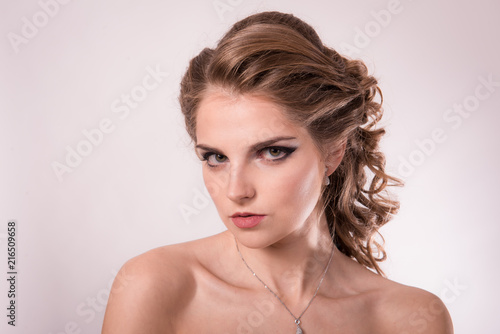 Brown-haired woman with professional hair and make-up against a light background close-up.