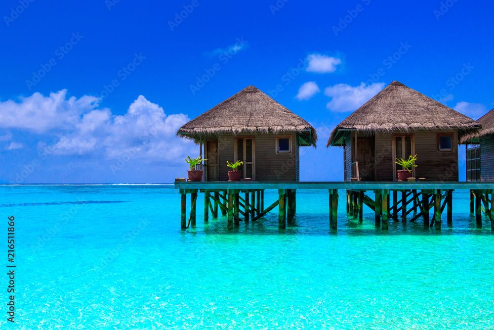 Water villas on wooden pier in turquoise ocean on the white sand beach