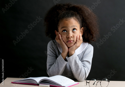 little beautiful girl is trying to learn the poem by heart. dreaming school girl sitting at the table with books and glasses photo