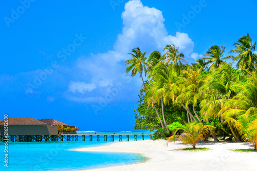 Fototapeta Naklejka Na Ścianę i Meble -  Water villas in turquoise ocean and wooden walkway leading to the island with white beach and palm trees