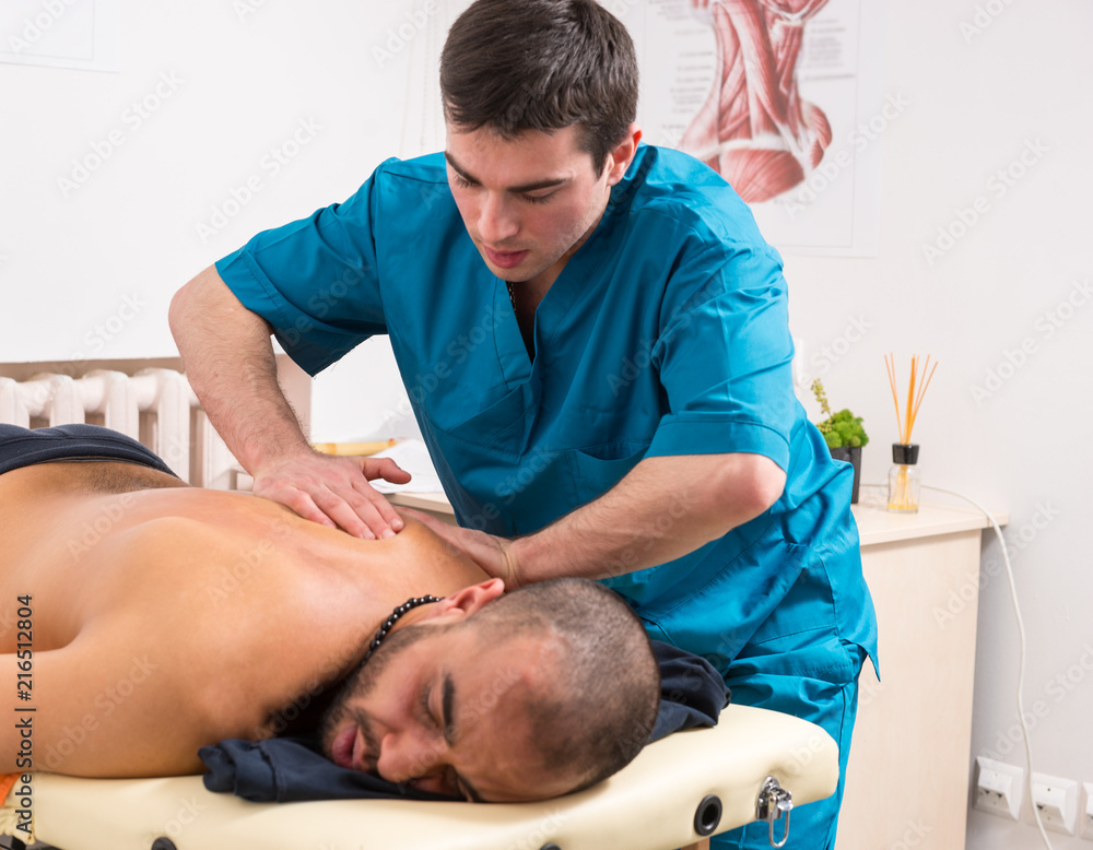 Masseur kneading the back muscles of a client Masseur kneading the back muscles of a client