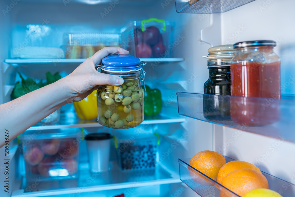 Hand reaching for jar with olives in fridge
