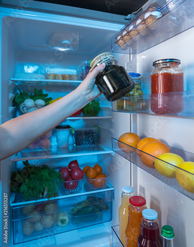 Hand reaching for jar of preserves in fridge