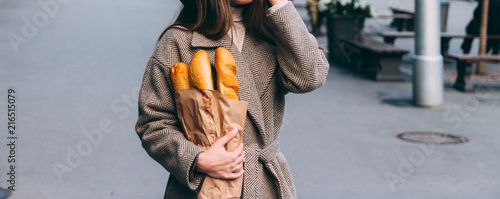 Cuadro en lienzo a girl in a coat and hat holds a bag with baguettes, bread, a loaf, on the street