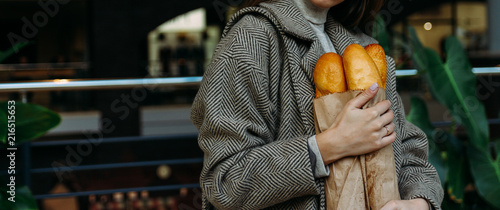 a girl in a coat is standing in a store with a baguette bag, breakfast, shopping, going to a grocery store.behind plants and market