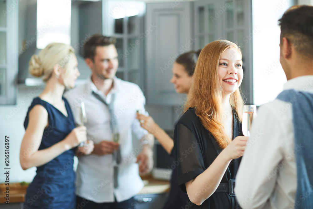Happy girl with flute of champagne talking to her boyfriend at party on background of friends Happy girl with flute of champagne talking to her boyfriend at party on background of friends