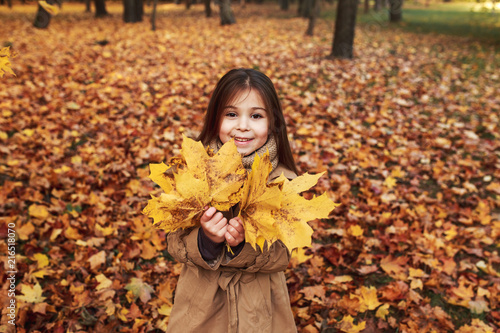 Closeup portrait of cute adorable smiling little caucasian girl child standing in autumn fall park outside  looking in camera 
