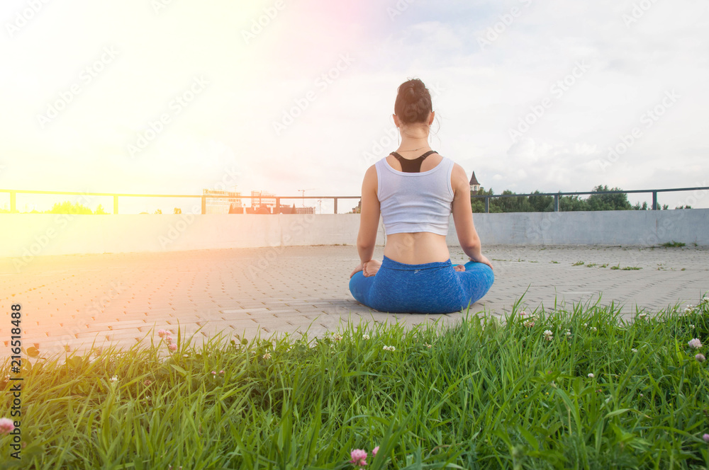 Young pretty woman practices yoga and meditates on the sunny embankment of the river