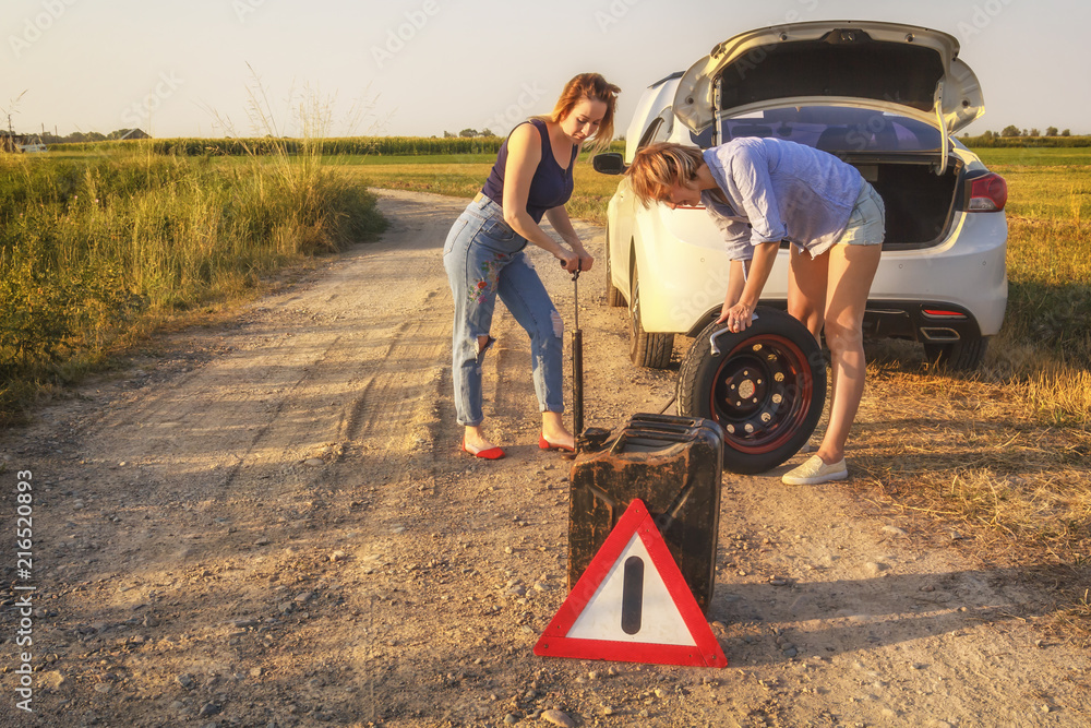 Two beautiful girls repair a car wheel on a country road in the rays of sunset. Tinted. Copy space Two beautiful girls repair a car wheel on a country road in the rays of sunset. Tinted. Copy space