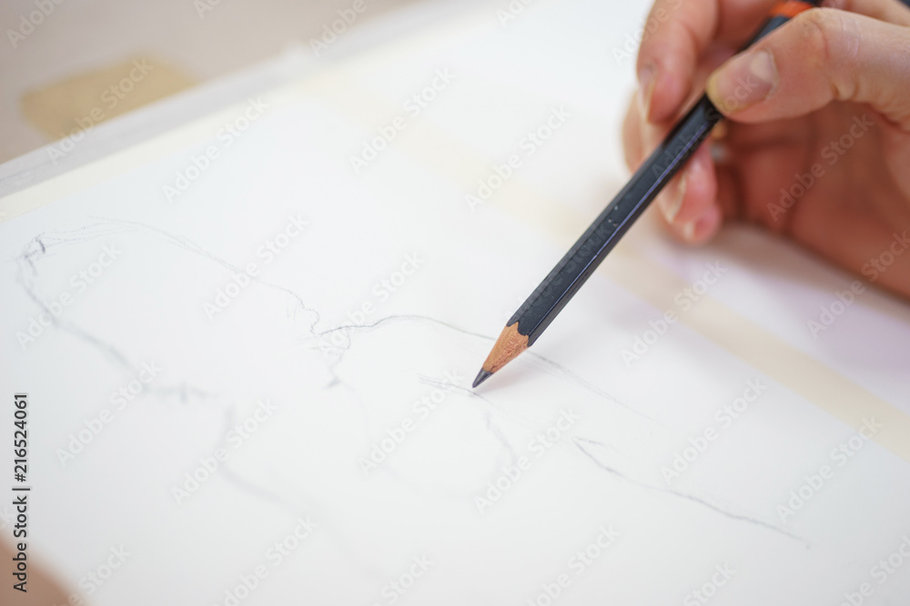 Hand of an artist with a pencil close-up while drawing a sketch on clean paper. Hand of an artist with a pencil close-up while drawing a sketch on clean paper.