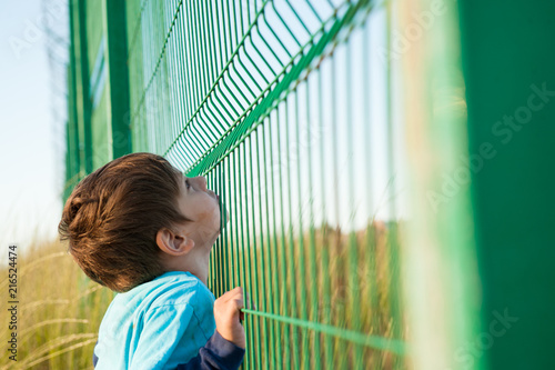 poor little caucasian child refugee looking up for freedom holding cage fence on border photo