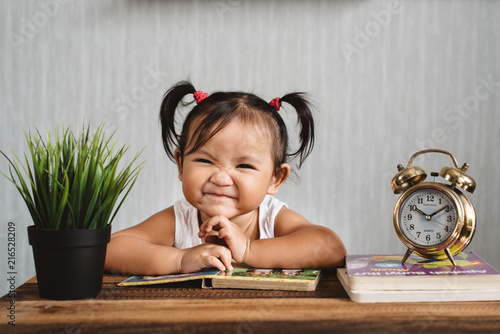 cute little asian baby toddler making funny face with books and alarm clock. child growth and learning concept