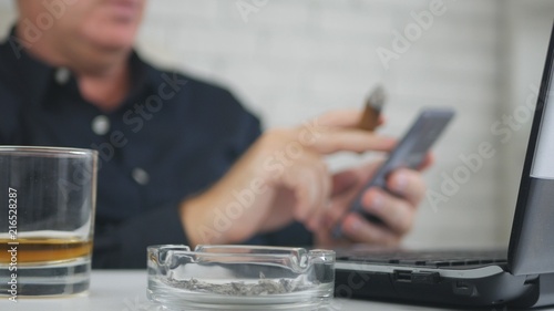 Blurred Image with a Businessman Smoking Cigar Drinking Whisky and Using Cellpho