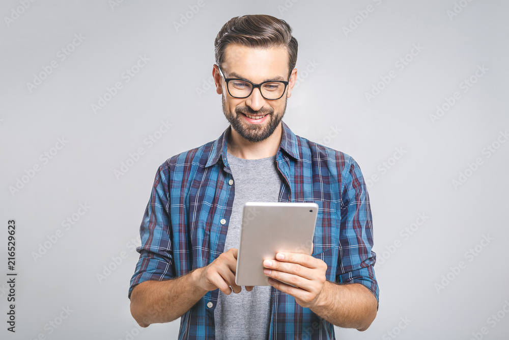 © denis_vermenko - Happy young man in plaid shirt standing and using tablet over grey background