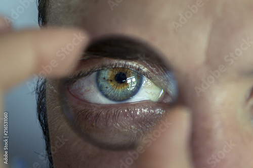 Portrait of a young man with a magnigying glass in front of his eye to show the beautiful details of it photo