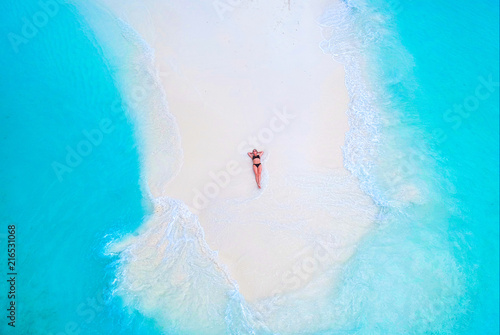 Beautiful woman tans on sandbank surrounded by turquoise ocean from above photo