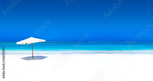 Parasol on white beach with turquoise ocean and cloudless sky