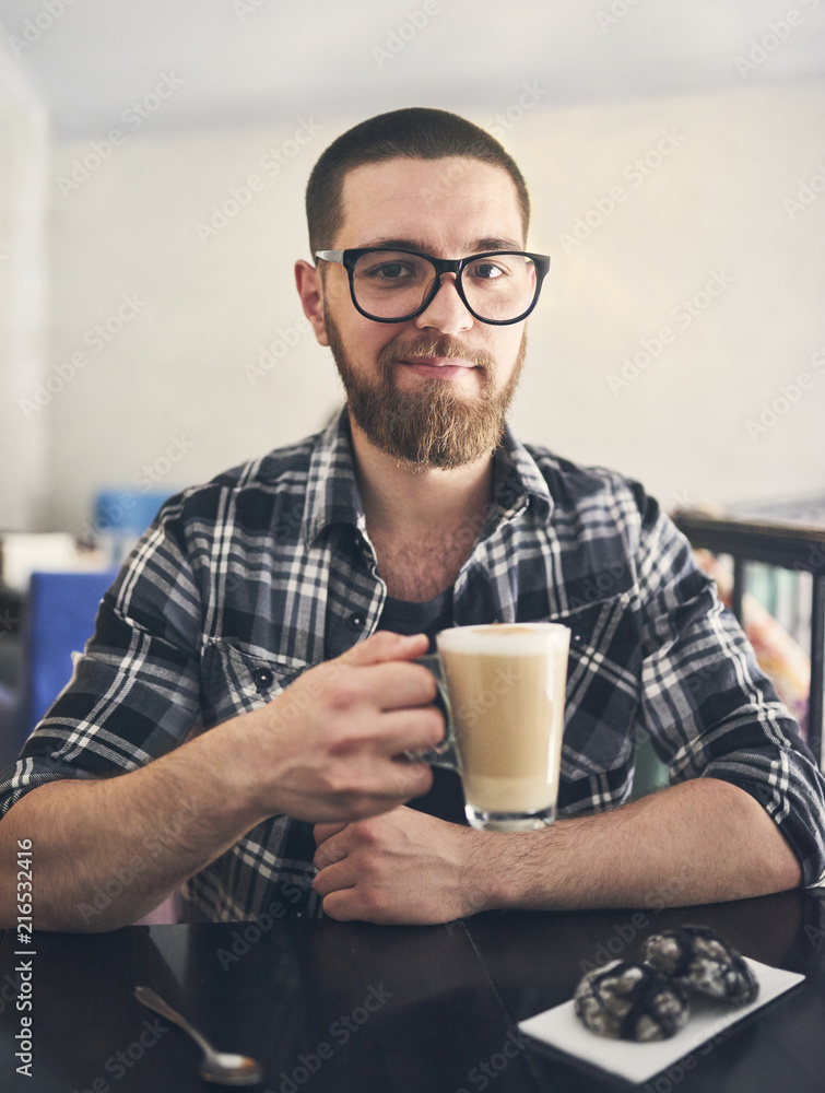 Smiling bearded man in glasses holding a glass with coffee